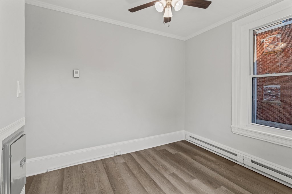 A room with a ceiling fan and a window with a brick wall view.