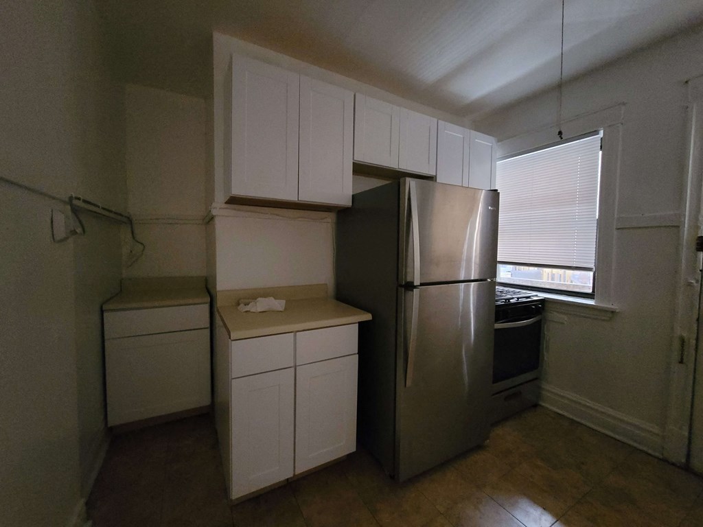 an empty kitchen with white cabinets and a stainless steel refrigerator