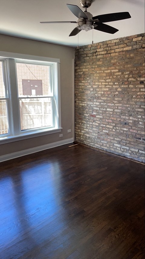 an empty living room with a brick wall and a ceiling fan