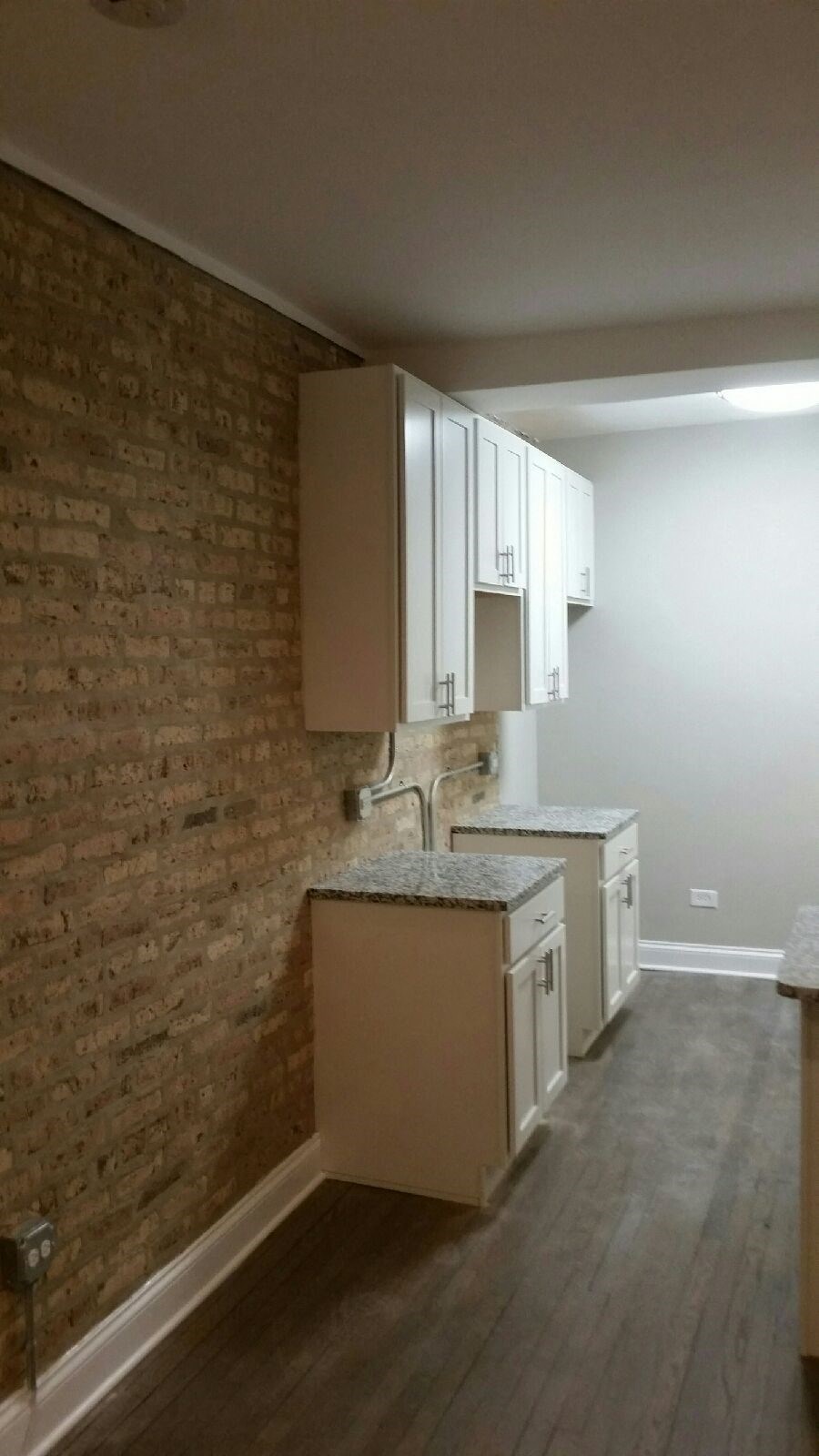 a small kitchen with white cabinets and a brick wall