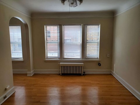 a living room with wood floors and a radiator and three windows