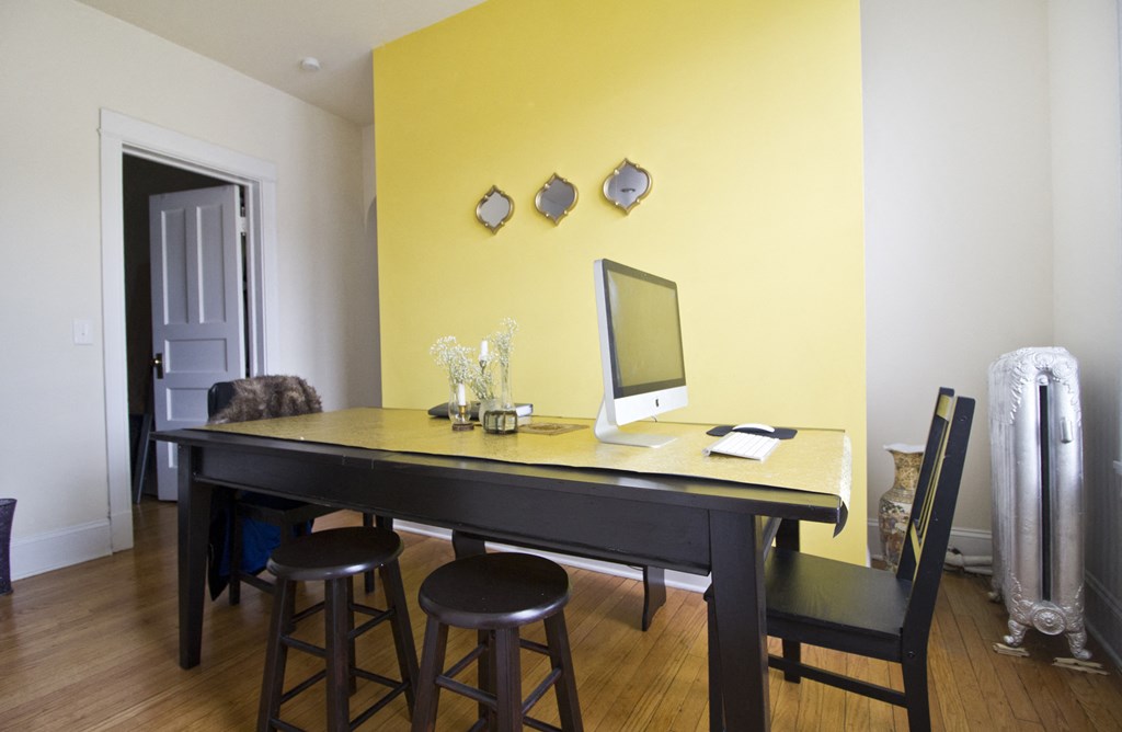 a home office with a black desk and a yellow wall