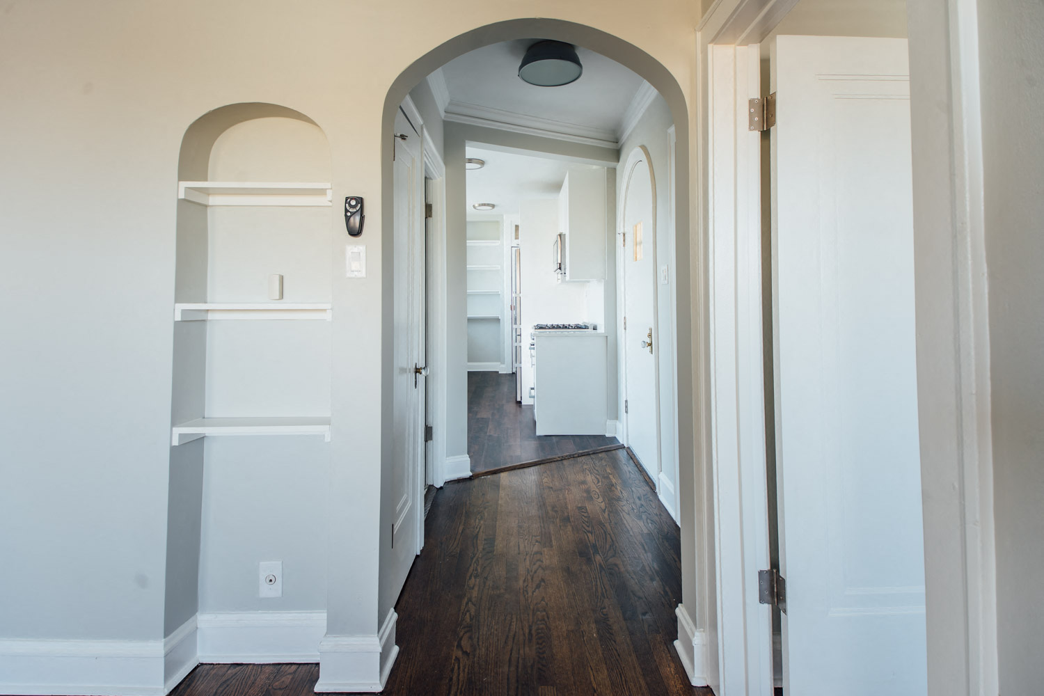 a hallway with white walls and wooden floors and an arched door way