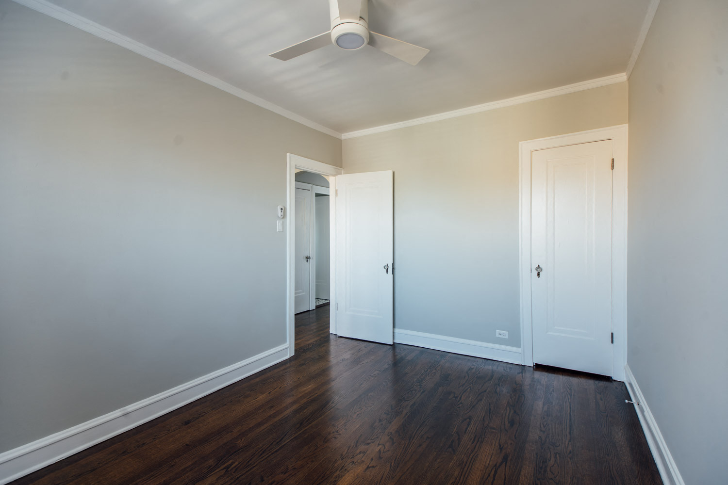 a bedroom with white walls and wood floors and a ceiling fan