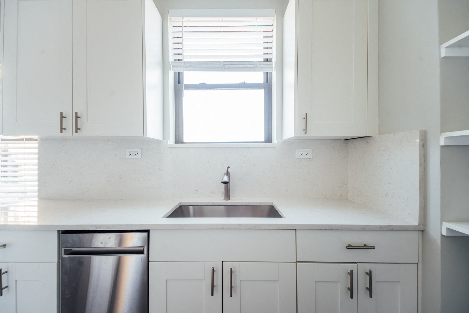 an empty kitchen with white cabinets and a window above the sink