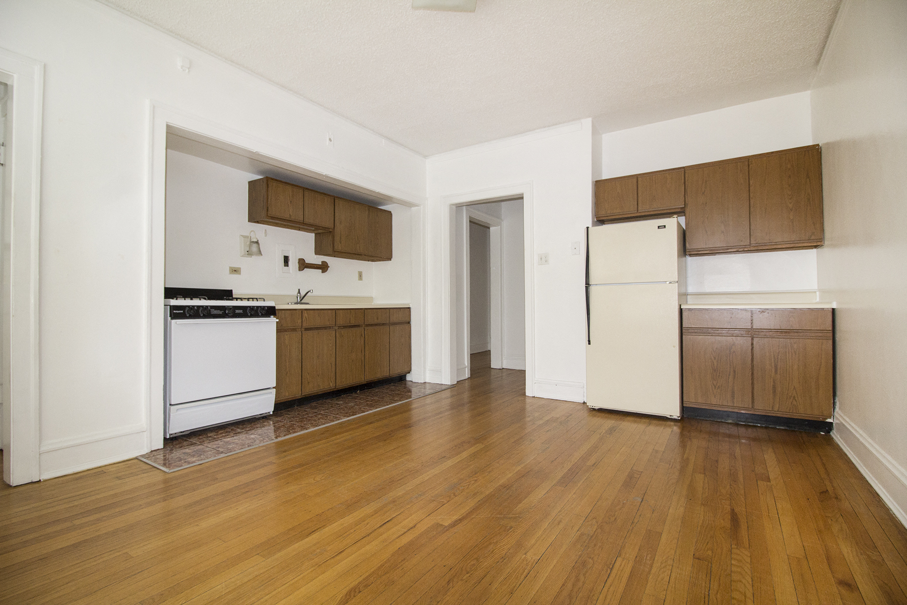an empty kitchen with white appliances and wooden floors