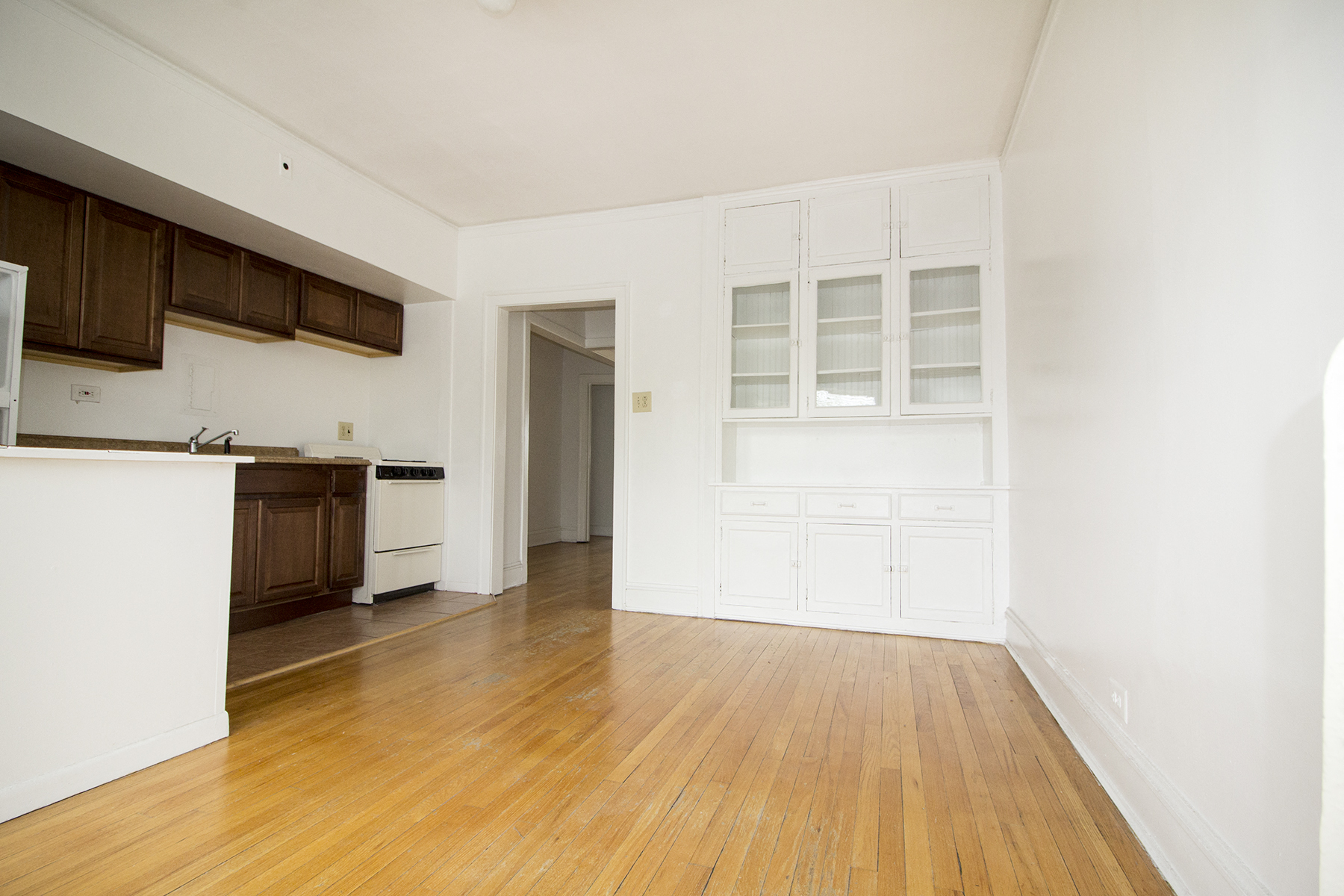 an empty living room and kitchen with white walls and wood floors