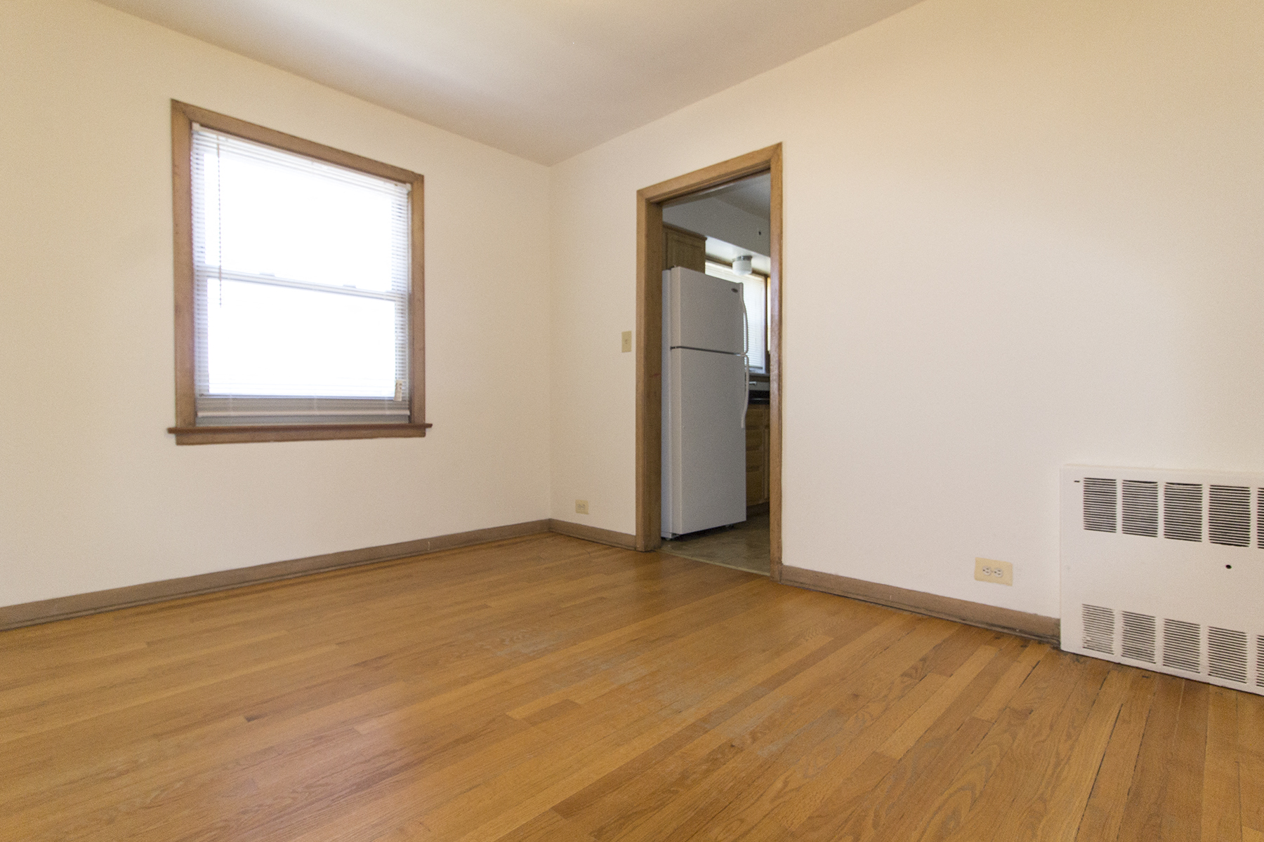 an empty room with wood floors and a window and a refrigerator