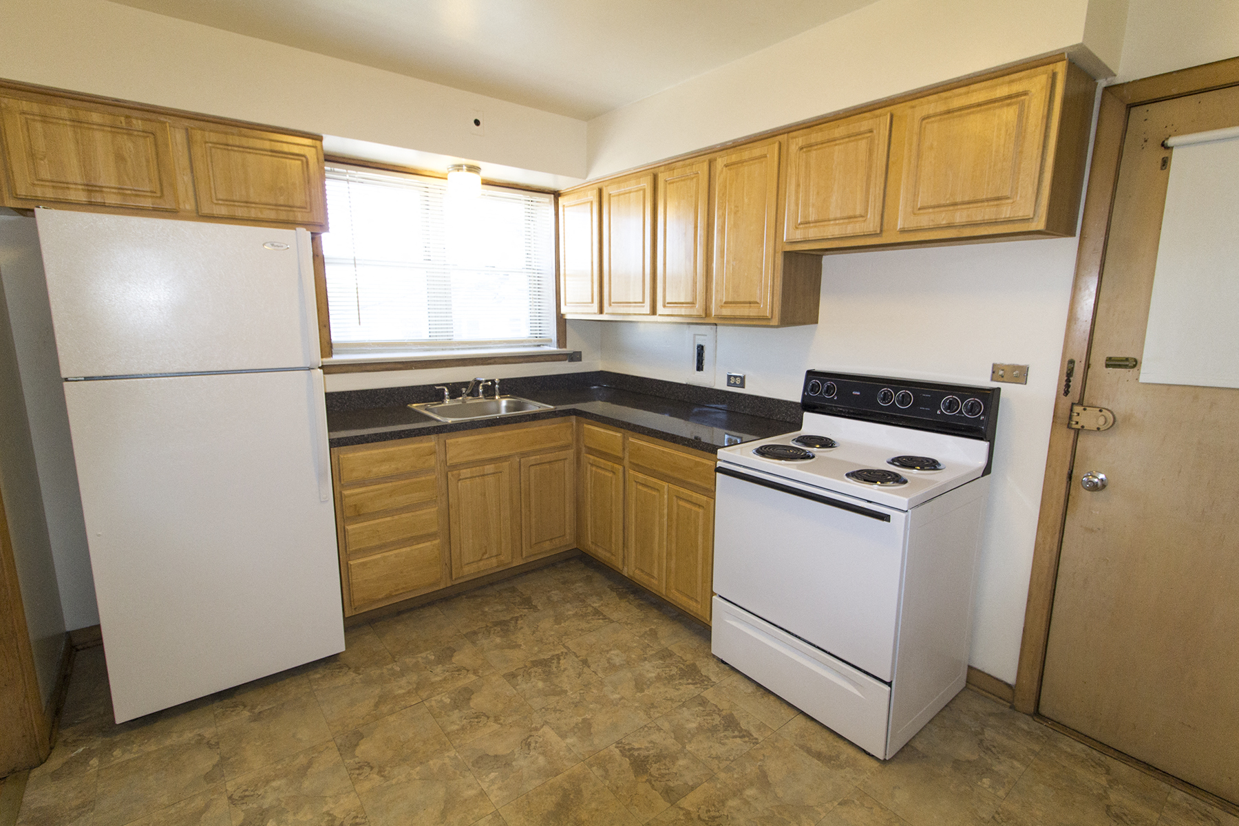 an empty kitchen with white appliances and wooden cabinets