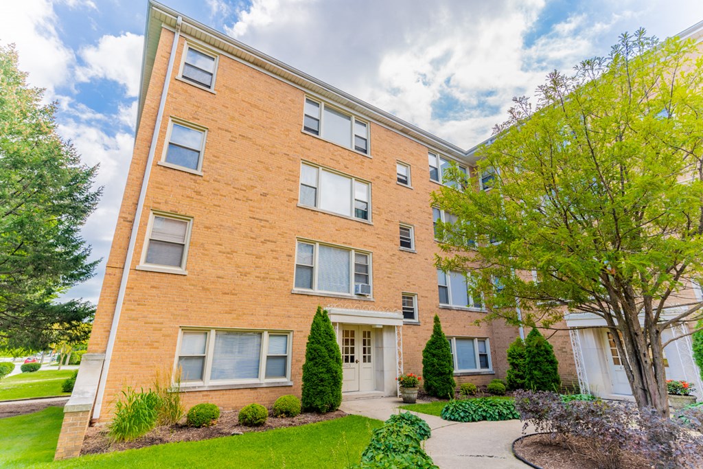 exterior view of a brick apartment building with a sidewalk and grass