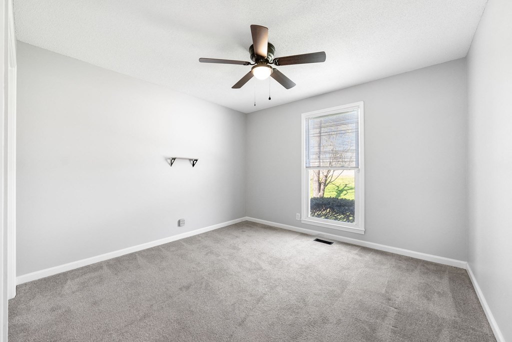 an empty living room with a ceiling fan and a window