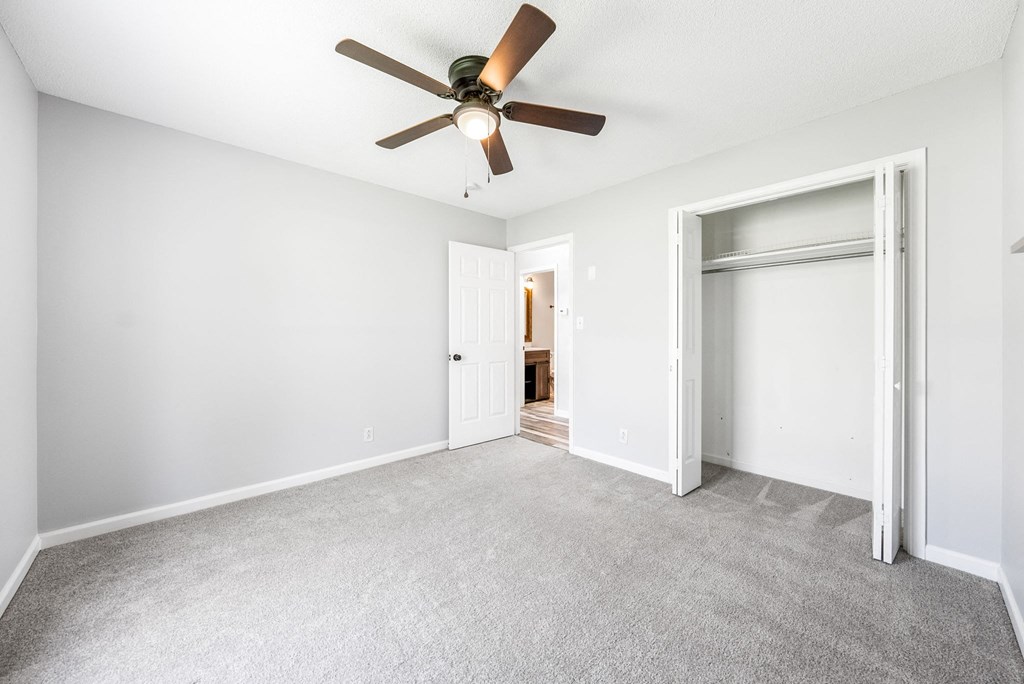 an empty living room with a ceiling fan and a closet