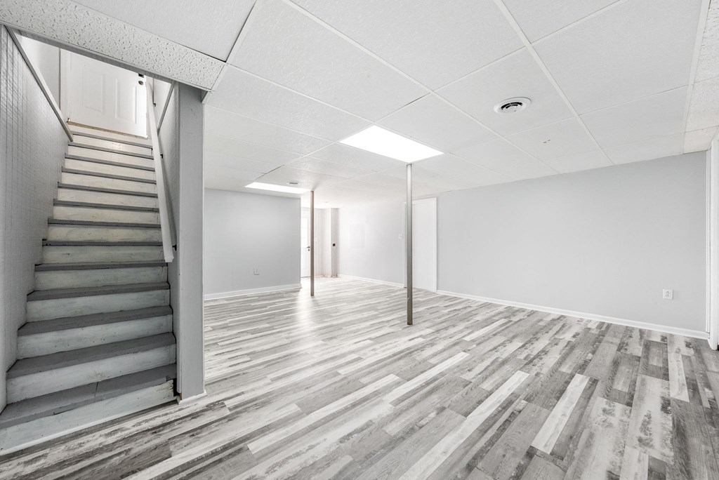 the living room and staircase of a house with white walls and wood floors
