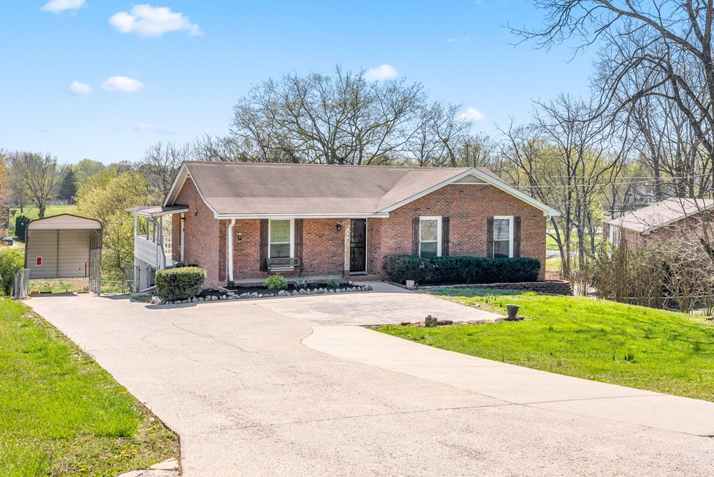 a small brick house with a driveway and a lawn