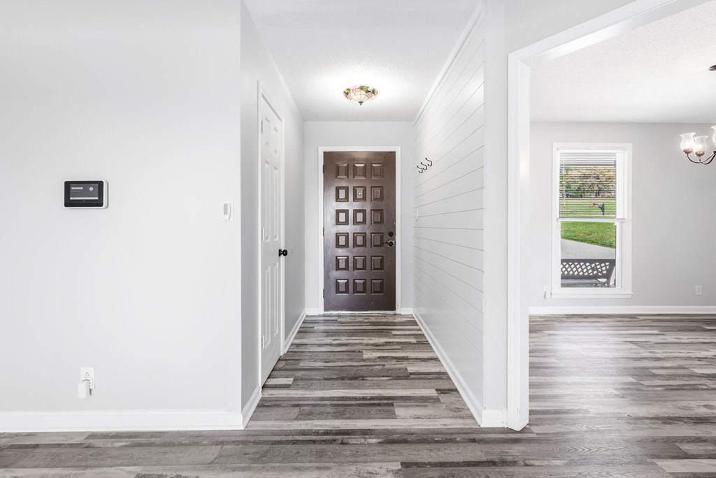 a hallway with white walls and wooden floors and a brown door