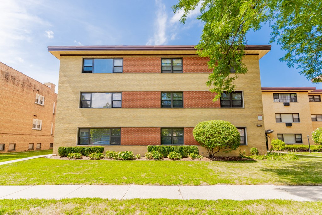a brick apartment building with a lawn and a tree in front of it