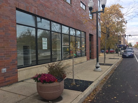 A brick building with a sign that says "For Lease" is on the corner of a street.