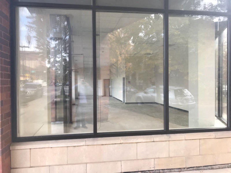 A view of a street through a window with a reflection of a car and a building.