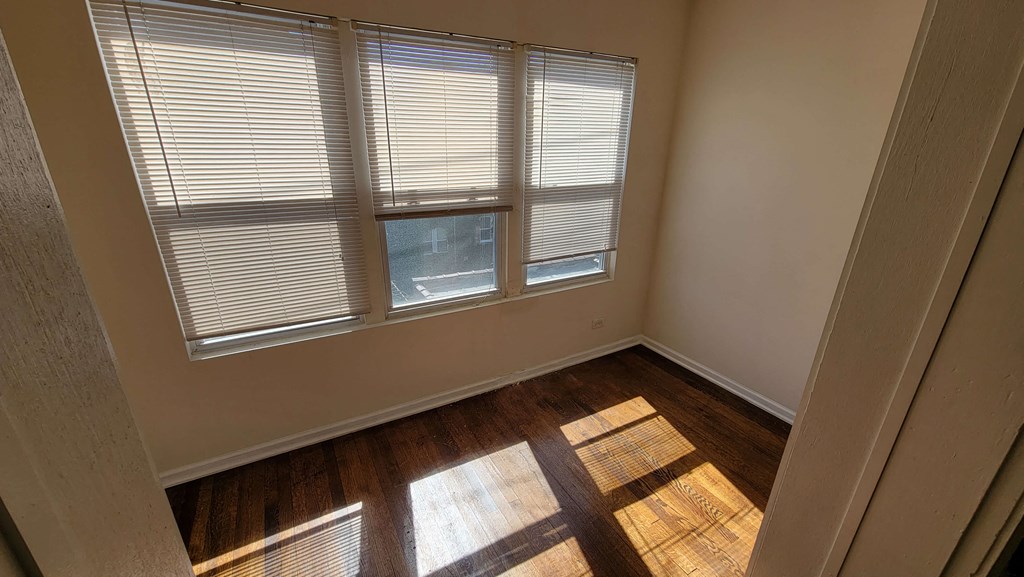 a bedroom with three windows and wood floors