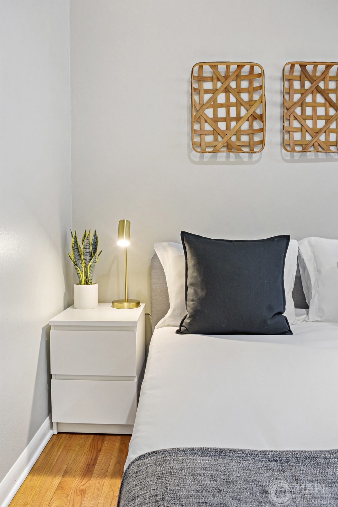 a bedroom with a bed with a black pillow and a night stand with a plant