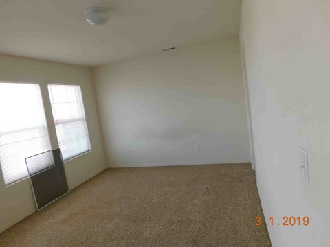 A room with a carpet floor, a window with blinds, and a wall with a date stamp.