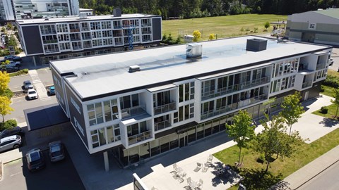 A modern building with a flat roof and a parking lot in front.