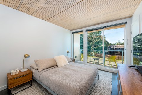 A bedroom with a bed, nightstand, and a window overlooking a backyard.