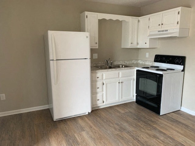 A white refrigerator is in a kitchen with wooden floors.