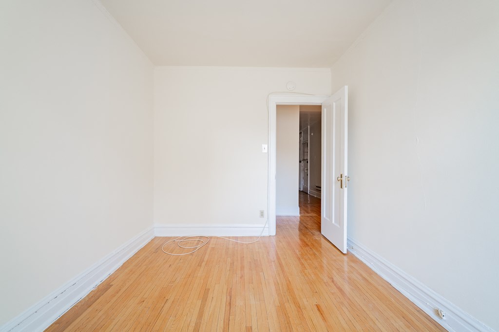 a bedroom with white walls and wood floors and a door to a hallway