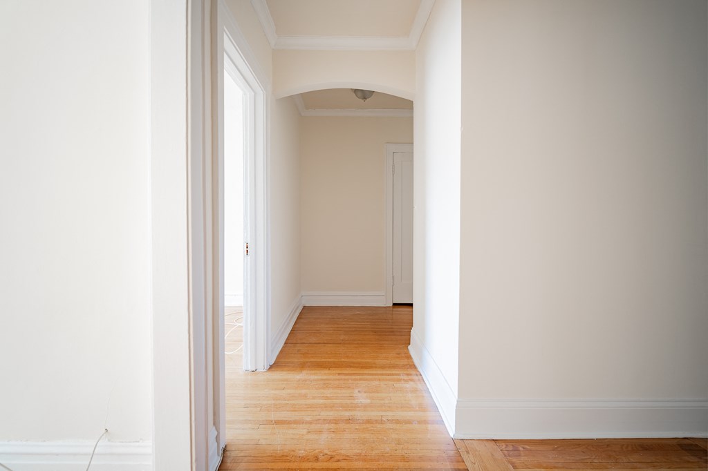 a hallway with white walls and wooden floors and a white door