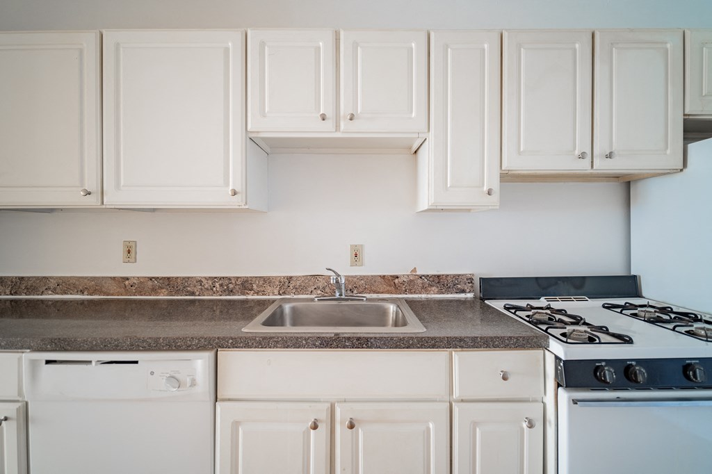 an empty kitchen with white cabinets and a stove and sink