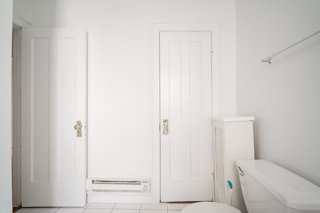 a white bathroom with two doors and a toilet