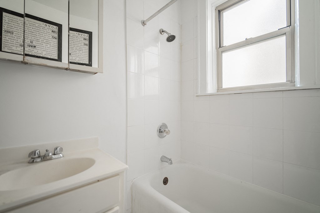 a white bathroom with a sink and tub and a window