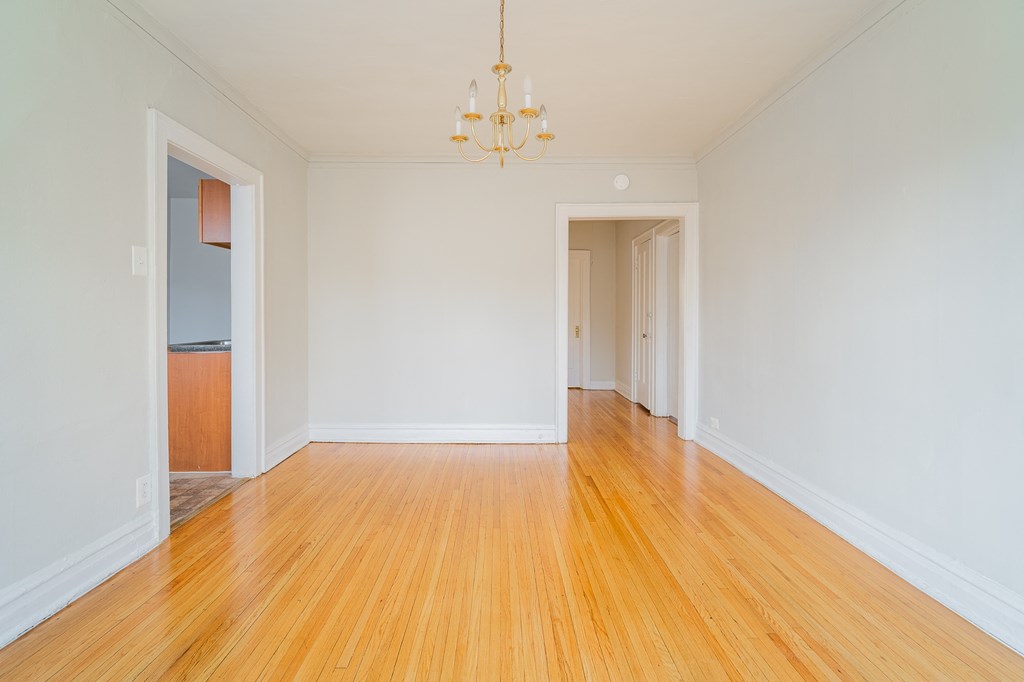 an empty living room with white walls and wooden floors and a chandelier