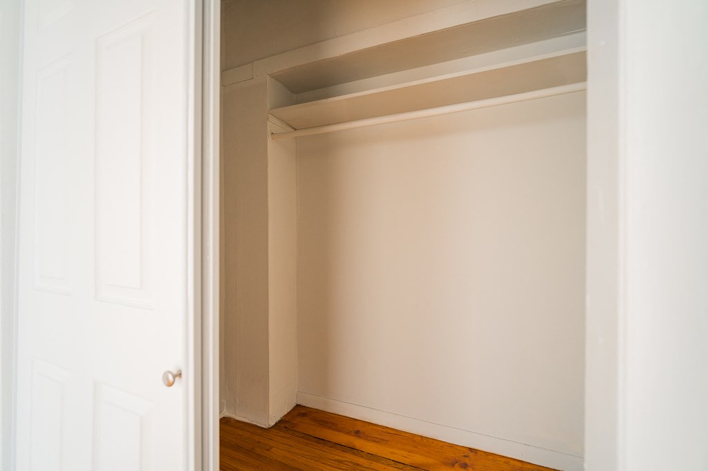 a small room with a white wall and a wooden floor and a closet
