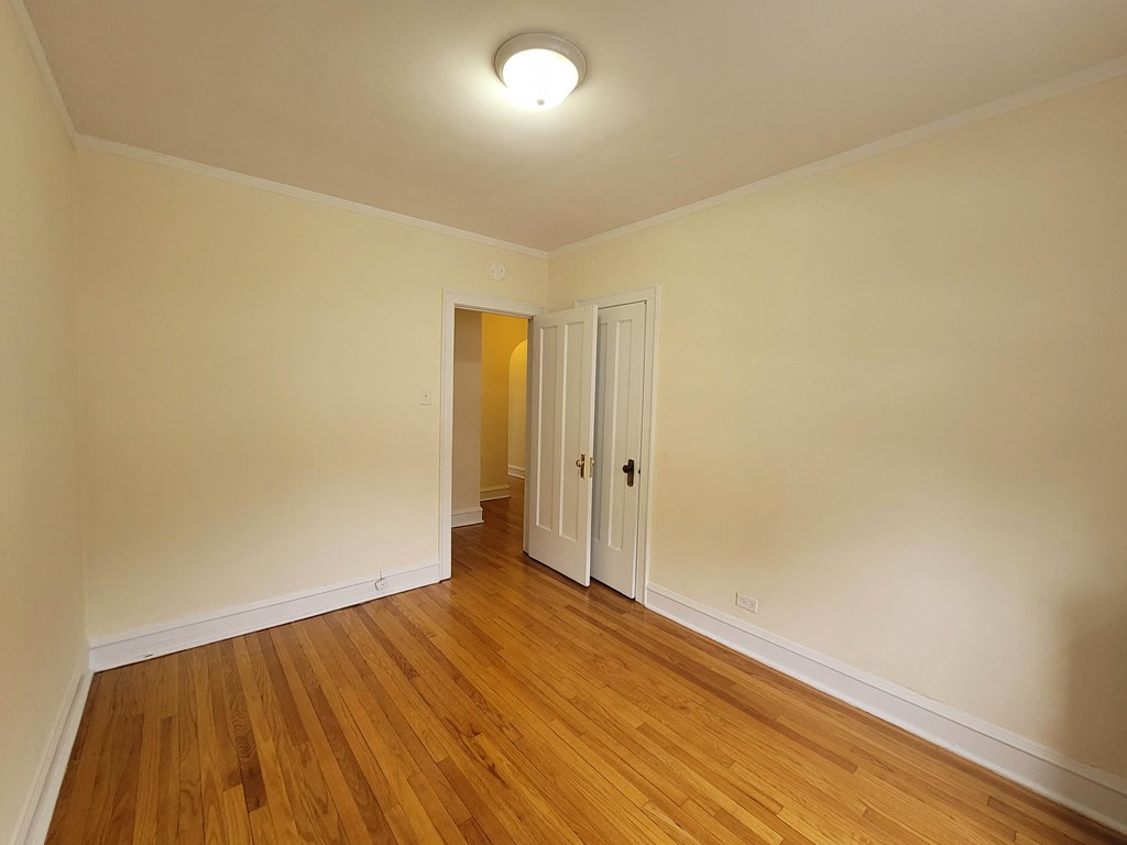 a bedroom with wood floors and white walls and a door to a hallway