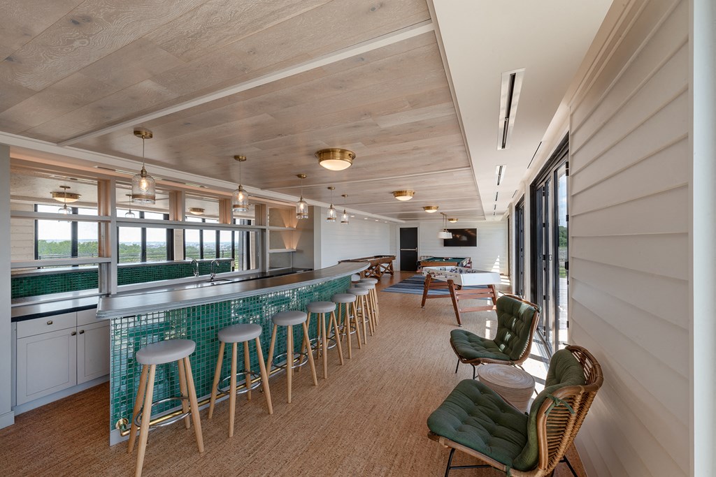 a bar with green chairs and stools in a room with windows