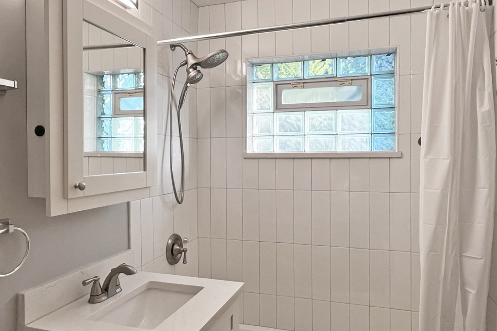 A white bathroom with a sink, mirror, and shower.