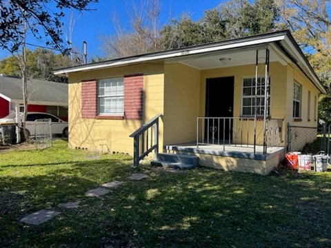 a small yellow house with a porch and a fence