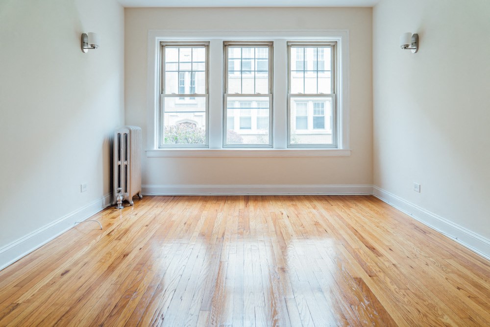an empty room with wooden floors and three windows