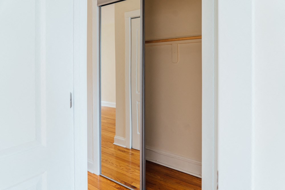 a mirrored closet door in a room with wood floors and white walls