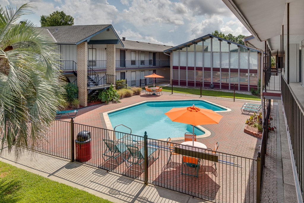 a swimming pool in a courtyard with tables and umbrellas