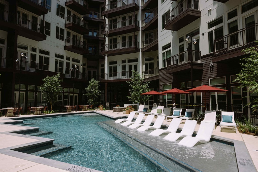 a pool with white lounge chairs in front of an apartment building