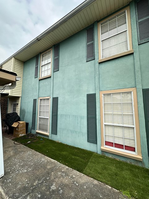 the side of a blue house with green shutters and grass