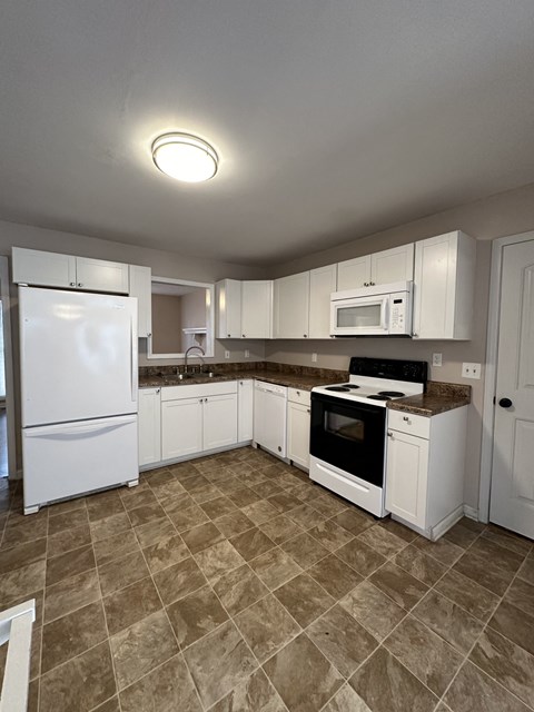 an empty kitchen with white appliances and white cabinets
