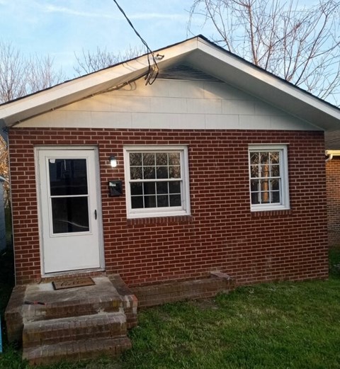 A small red brick house with a white door and windows.