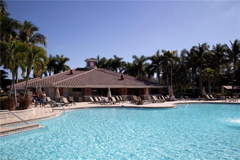 a resort pool with chairs and a building with palm trees
