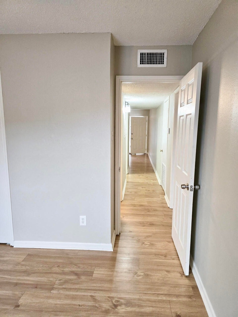 a hallway with white walls and wood floors and a white door