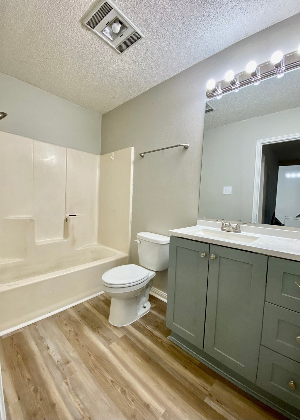 A white toilet sits in a bathroom with wooden floors and white walls.
