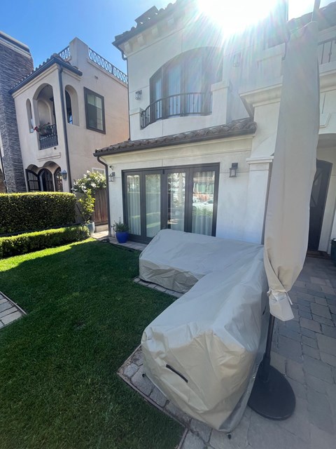 A patio with a white umbrella and a white chair covered in a white cloth.
